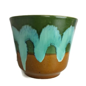 May include: A green and brown ceramic planter with a light blue glaze. The glaze has a dripping effect, creating a unique and artistic design.