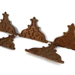 May include: A collection of six brown, ornate wooden decorative corner brackets. Each bracket features a detailed, symmetrical design with scrolling and floral elements. The brackets are arranged on a white background, showcasing their intricate carvings.