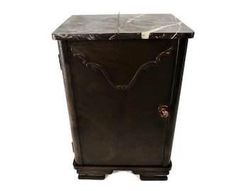 May include: A dark brown wooden cabinet featuring a rectangular top surface made of dark brown and white veined marble. The front door includes a decorative carved wooden accent at the top and a small round knob. The cabinet rests on a tiered base.