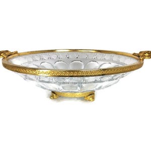 May include: A clear glass bowl with a gold rim and ornate handles. The bowl has a decorative, cut-glass pattern and sits on three gold feet.