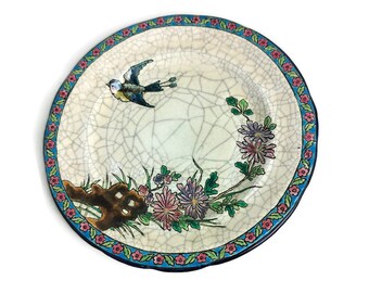 Pode incluir: Um prato de cerâmica branca com um desenho floral azul e rosa e um pássaro azul. O prato tem um esmalte craquelado.