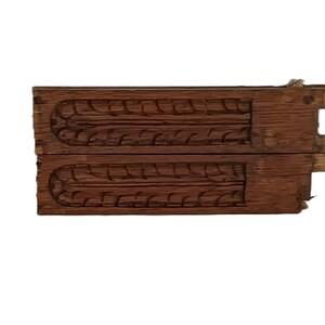 May include: Two-piece wooden mold with carved leaf-like patterns. The dark brown wood shows signs of age and wear, with visible imperfections. The mold is likely for creating decorative items.