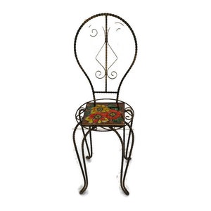 Puede incluir: Una silla de metal negro con un asiento de azulejos con estampado floral. La silla tiene un respaldo alto con un diseño decorativo.