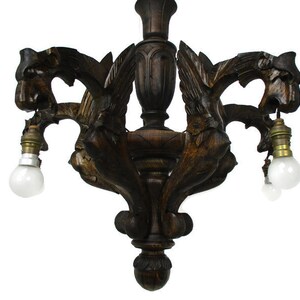 Pode incluir: Um candeeiro de teto de madeira castanho escuro com quatro lâmpadas e um design decorativo de criaturas aladas.