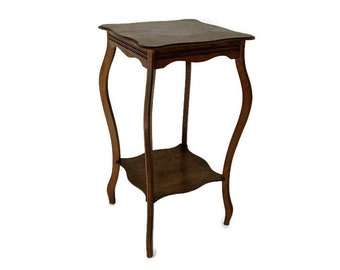Puede incluir: Una mesa auxiliar de madera marrón oscuro con una parte superior festoneada y dos estantes. La mesa tiene un diseño curvo y adornado en las patas.