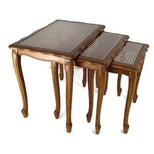 Op de afbeelding: Een set van drie nesttafels met een houten frame en gevlochten rieten bladen. De tafels zijn bruin en hebben een verweerde afwerking.