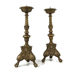 Puede incluir: Un par de candelabros antiguos de latón con detalles ornamentados y tres patas cada uno.