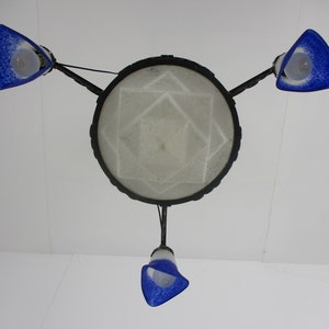 May include: A ceiling light fixture with a central circular shade and three blue glass shades. The central shade has a geometric pattern. The blue shades are triangular and speckled. The fixture is suspended from the ceiling.