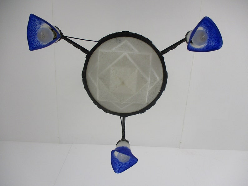 May include: A ceiling light fixture with a central circular shade and three blue glass shades. The central shade has a geometric pattern. The blue shades are triangular and speckled. The fixture is suspended from the ceiling.