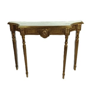 May include: A gold-colored console table with a marble top. The table has ornate detailing, including floral carvings and a central medallion. The legs are slender and fluted. The table is designed to be placed against a wall.