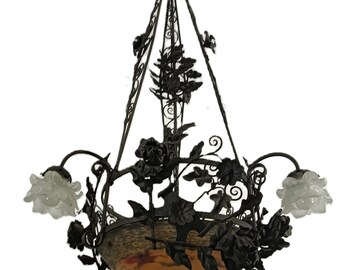 May include: An antique chandelier with a dark bronze finish, featuring intricate floral and leaf details. The chandelier has a central bowl with an orange and brown mottled design, and two frosted glass flower-shaped light fixtures.