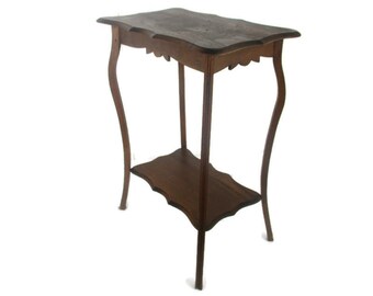 Puede incluir: Una mesa auxiliar de estilo antiguo, de color marrón oscuro, con un borde festoneado en la parte superior e inferior. La mesa tiene patas curvas y mide aproximadamente 76 cm de altura.