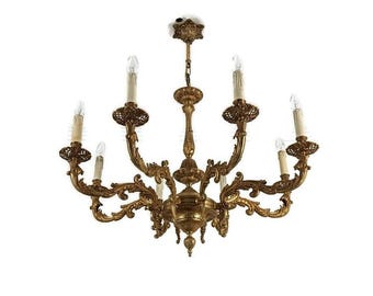 May include: Ornate gold chandelier with multiple curved arms, each holding a light bulb. The chandelier features intricate scrollwork and decorative elements, creating a classic and elegant design. The fixture is suspended from a central point.
