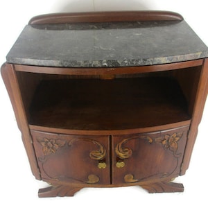 Può includere: Un comodino in legno scuro con un piano in marmo e dettagli floreali intagliati. Il comodino ha due ante e uno scaffale.