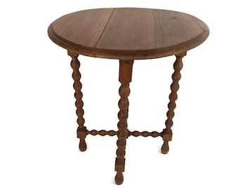 May include: A small, round wooden table with a dark brown finish. The table has a circular top and three legs with a turned, bobbin design. The table is likely an antique or vintage piece, suitable for a living room or bedroom. The table's diameter is approximately 60 cm.