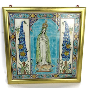 May include: Framed ceramic tile art featuring a religious figure with a crown, wearing a green cloak, and standing on a floral base. The artwork is set against a light blue background and framed in gold. The artwork is a religious theme.