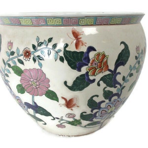 May include: A white ceramic planter with a floral design. The planter features pink, orange, blue, and green flowers with butterflies. The planter has a white background with a blue and green border.