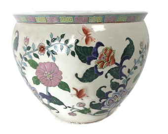 Könnte beinhalten: Ein weißer Keramiktopf mit Blumenmuster. Der Topf zeigt rosa, orange, blaue und grüne Blumen mit Schmetterlingen. Der Topf hat einen weißen Hintergrund mit einem blauen und grünen Rand.