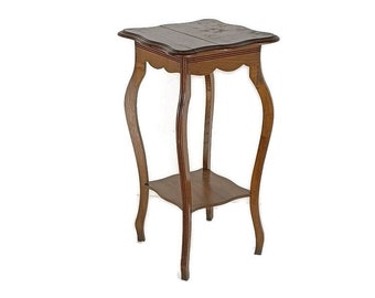 Puede incluir: Un soporte para plantas de madera marrón oscuro con una parte superior festoneada y un estante inferior. El soporte tiene cuatro patas con un diseño curvo.