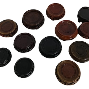 Puede incluir: Una colección de soportes de exhibición de madera en varios tonos de marrón y negro. Los soportes son redondos con un centro empotrado y bordes decorativos. Algunos tienen un acabado brillante, otros son mate.