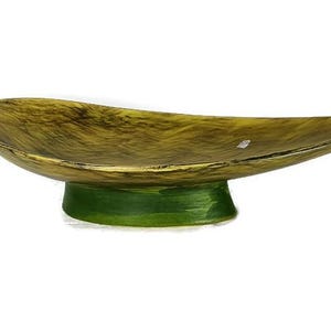 May include: A decorative bowl in the shape of a leaf, featuring a textured, golden-brown finish. It rests on a bright green, cylindrical base. The design is organic and elegant, suitable for display or serving.