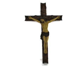 May include: A wooden crucifix featuring a carved figure of Jesus Christ. The cross is dark brown, with a textured surface. The figure is painted in shades of tan and brown, with a dark cloth draped around the waist. The cross has the letters INRI at the top.