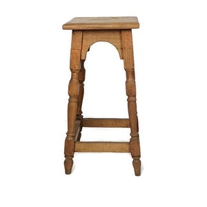 May include: A vintage wooden stool with a square seat and turned legs. The stool has a light brown finish and a simple, classic design. The legs are connected by a horizontal stretcher for added stability.