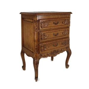 Puede incluir: Un cofre de madera de tres cajones con tallas ornamentadas y herrajes de latón. El cofre está acabado en un rico color marrón y tiene patas cabriole.