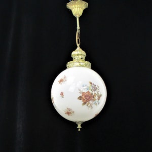 May include: A vintage globe pendant light with a white glass shade adorned with floral patterns in shades of red, brown, and blue. The light fixture features brass-colored metal accents and a decorative top.