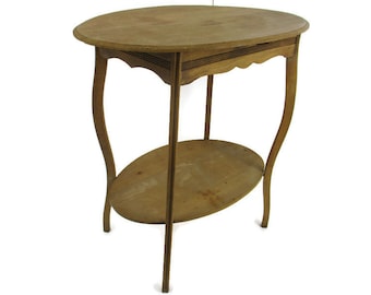 Puede incluir: Una mesa auxiliar de madera vintage con una tapa ovalada y un estante inferior ovalado. La mesa tiene patas curvas y un acabado marrón claro. La mesa mide aproximadamente 71 cm de alto.