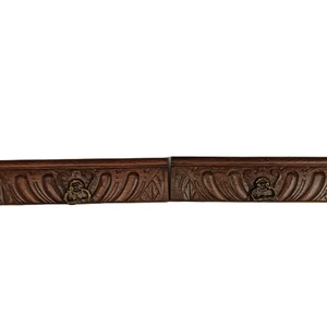 May include: Two rectangular, dark brown wooden boxes with ornate carvings and a small brass figure on the front. The boxes are side-by-side, with a white background.