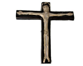 May include: A religious crucifix with a silver-colored figure of Jesus Christ against a black cross. The figure has outstretched arms and is centered on the cross. The cross is rectangular with a smooth surface.