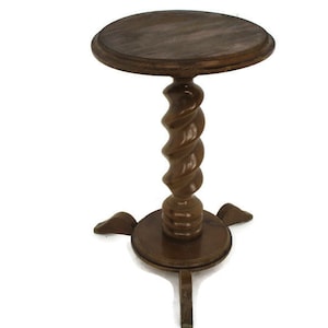 Op de afbeelding: Een kleine bruine houten bijzettafel met een rond blad, een centrale kolom met een gesneden spiraalvormig ontwerp en een ronde voet die wordt ondersteund door drie korte, gebogen pootjes die naar buiten toe uitsteken.