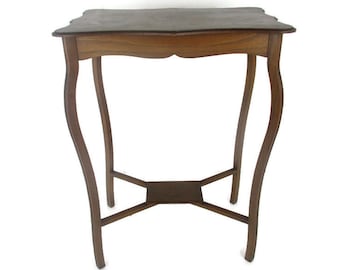 Puede incluir: Pequeña mesa auxiliar de madera antigua con acabado marrón oscuro. La mesa tiene una parte superior festoneada única y patas curvas. Una balda inferior proporciona almacenamiento adicional. La mesa mide unos 71 cm de alto.