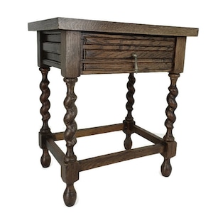 Puede incluir: Una mesa auxiliar de madera marrón oscuro con un solo cajón y un estante inferior. Las patas de la mesa son torneadas y tienen un diseño retorcido.