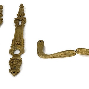 Puede incluir: Dos placas de puerta doradas adornadas con un ojo de cerradura y un par de manijas de puerta doradas a juego.