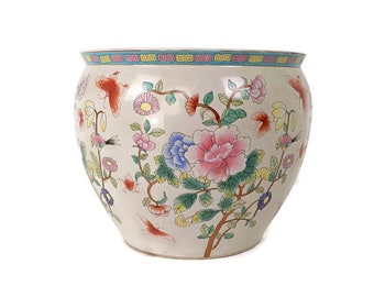 Könnte beinhalten: Ein weißer Keramiktopf mit Blumenmuster. Der Topf zeigt rosa, blaue, gelbe und grüne Blumen mit Schmetterlingen und Vögeln. Der Rand des Topfes hat ein blaues und gelbes geometrisches Muster.