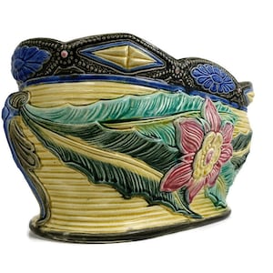 Op de afbeelding: Een grote, ovale keramische plantenbak met een geel, groen en roze bloemenmotief. De plantenbak heeft een verhoogde rand met een zwart en blauw geometrisch patroon.