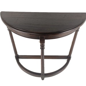 Puede incluir: Una mesa de color marrón oscuro, con forma de media luna, con una encimera curva y una base curva decorativa. La mesa tiene una sola pata central y dos patas anguladas, todas conectadas por un travesaño curvo. La mesa es de madera.