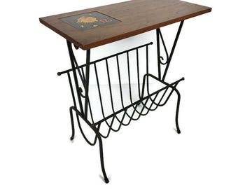 Puede incluir: Una mesa auxiliar vintage con una tapa de madera oscura y un revistero de metal negro. La mesa tiene una baldosa decorativa con un diseño dorado y marrón. La mesa tiene una estética moderna de mediados de siglo.