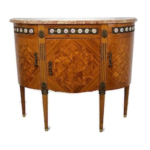 Può includere: Un mobile in legno a mezzaluna con piano in marmo. Il mobile presenta intricati motivi intarsiati, ferramenta decorativa e accenti floreali. Ha quattro gambe sottili e un fronte curvo, che mostra un design classico.