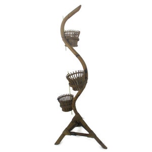 May include: A brown bamboo plant stand with three tiers. The stand is shaped like a tree trunk and has a triangular base.