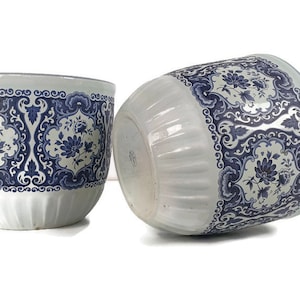 Puede incluir: Dos macetas de cerámica blanca con diseños florales azules y blancos. Las macetas tienen un diseño acanalado y son perfectas para agregar un toque de elegancia a la decoración de tu hogar.