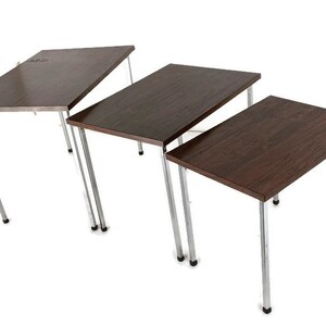 May include: Three rectangular nesting tables with dark brown wood-effect tops and chrome legs. The tables are of varying sizes, with the largest at the back and the smallest at the front. The legs are thin and angled.