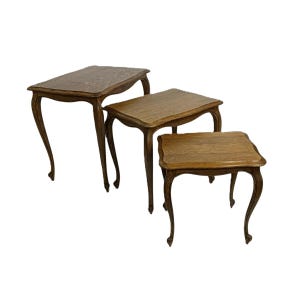 May include: Three antique wooden nesting tables. The tables have curved legs and rectangular tops. They are different sizes and have a warm, brown finish. The legs have a delicate, curved design.