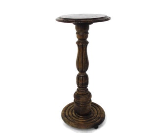 May include: A dark brown wooden pedestal table with a round top and a carved base. The table has a circular base with a decorative design.