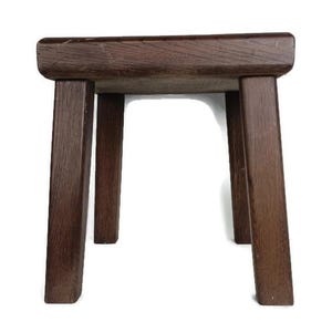 May include: A dark brown wooden stool with four legs. The stool is made of solid wood and has a simple, rustic design.