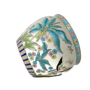 May include: A white ceramic planter with a blue, green, yellow, and pink floral design. The planter features a bird and butterflies.