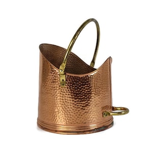 May include: A hammered copper log holder with a brass handle. The holder has a curved shape and a hammered texture.