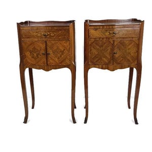 May include: A pair of antique wooden bedside cabinets with detailed marquetry. Each cabinet has a drawer, two doors, and elegant, curved legs. The wood is a warm brown, and the design is ornate and refined. The height is approximately 76 cm.